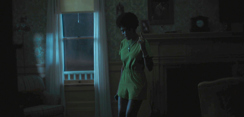 Keke Palmer in a yellow romper stands in a pitch black house and points up to the ceiling.