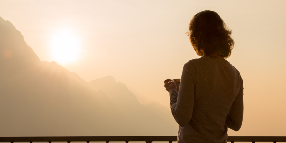 a woman stands in front of the sun rising over the mountains, contemplating her future