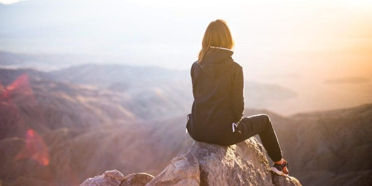 Woman sits on a rock, facing away from the camera, beholding a majestic view of a canyon