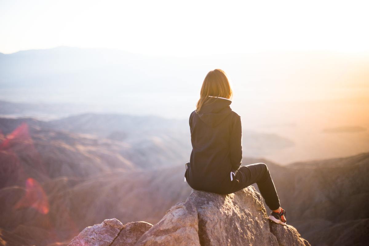 Woman sits on a rock, facing away from the camera, beholding a majestic view of a canyon