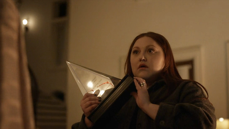 Gigi holds an award with blood on it and looks shocked