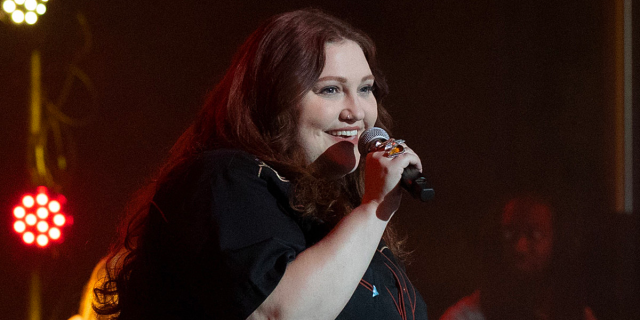 Beth Ditto as Gigi Roman on stage performing with a smile on her face