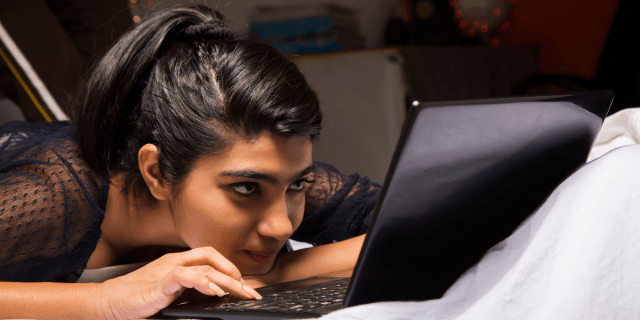 A young woman stares at a computer screen, smirking.