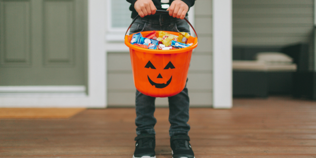 A child in a skeleton costume holds a trick or treat bucket