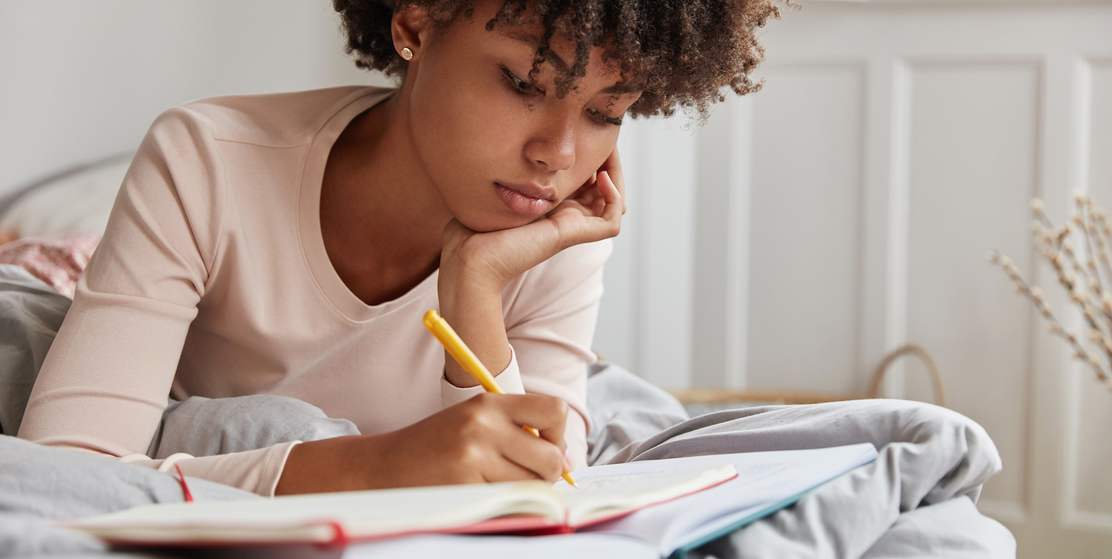 a young Black woman with short curly hair looks pensive as she writes in her journal