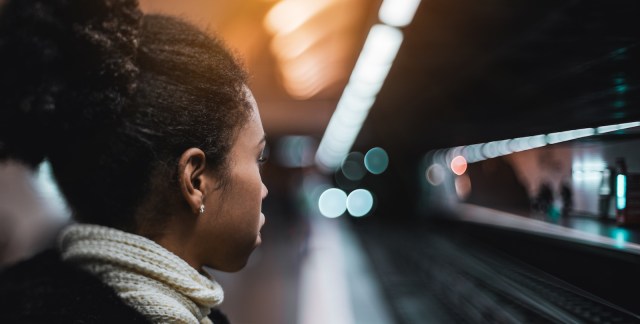 a young Black woman looking at an approaching train while standing on the metro station platform