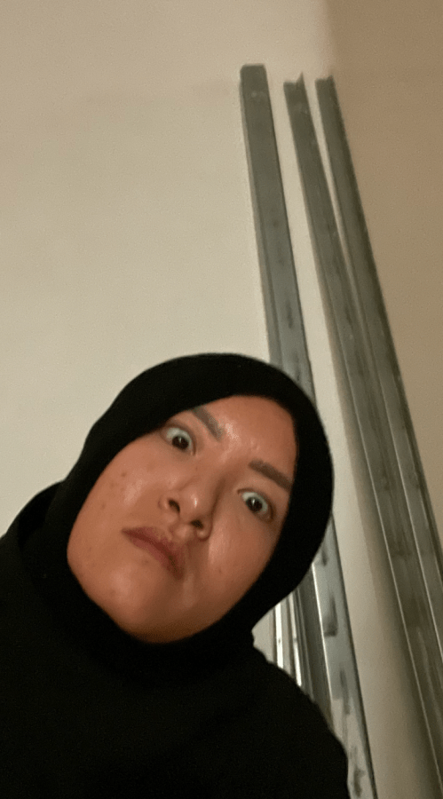 Viv, an Asian human with their head wrapped in a black cloth making an intense face in front of some metal brackets