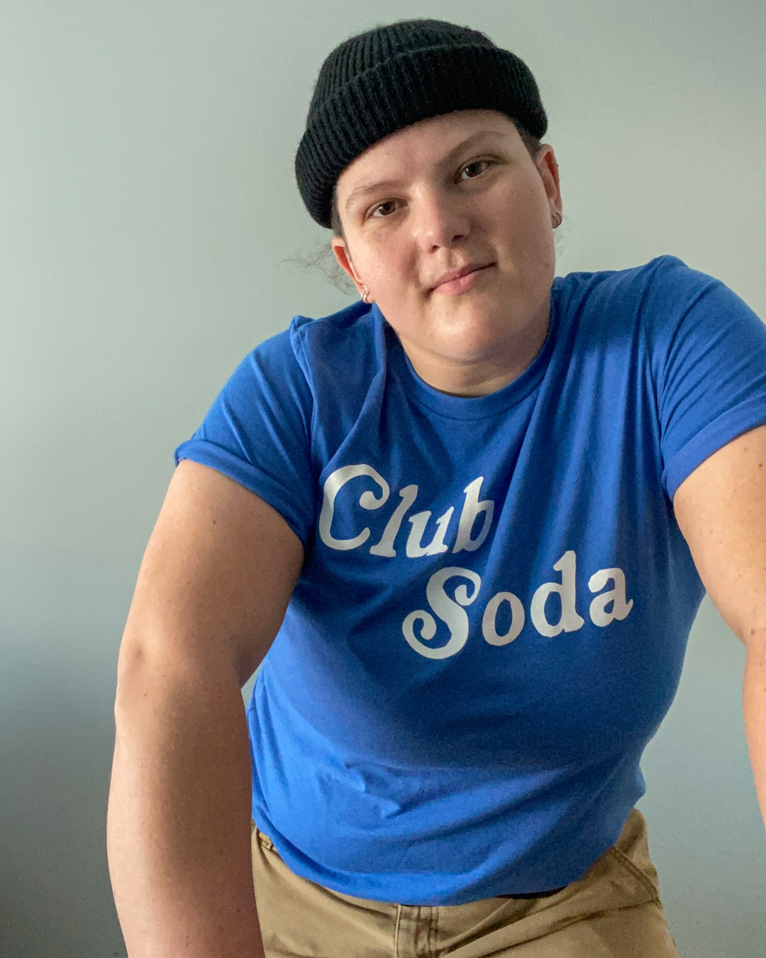 Model Jenny is 5'9" and a 38DDD, wearing size XL. The Club Soda Tee is a blue shirt in jersey blend. It has the words "Club Soda" printed in retro cursive typeface in off-white color. Club Soda represents those who are in the sober club.