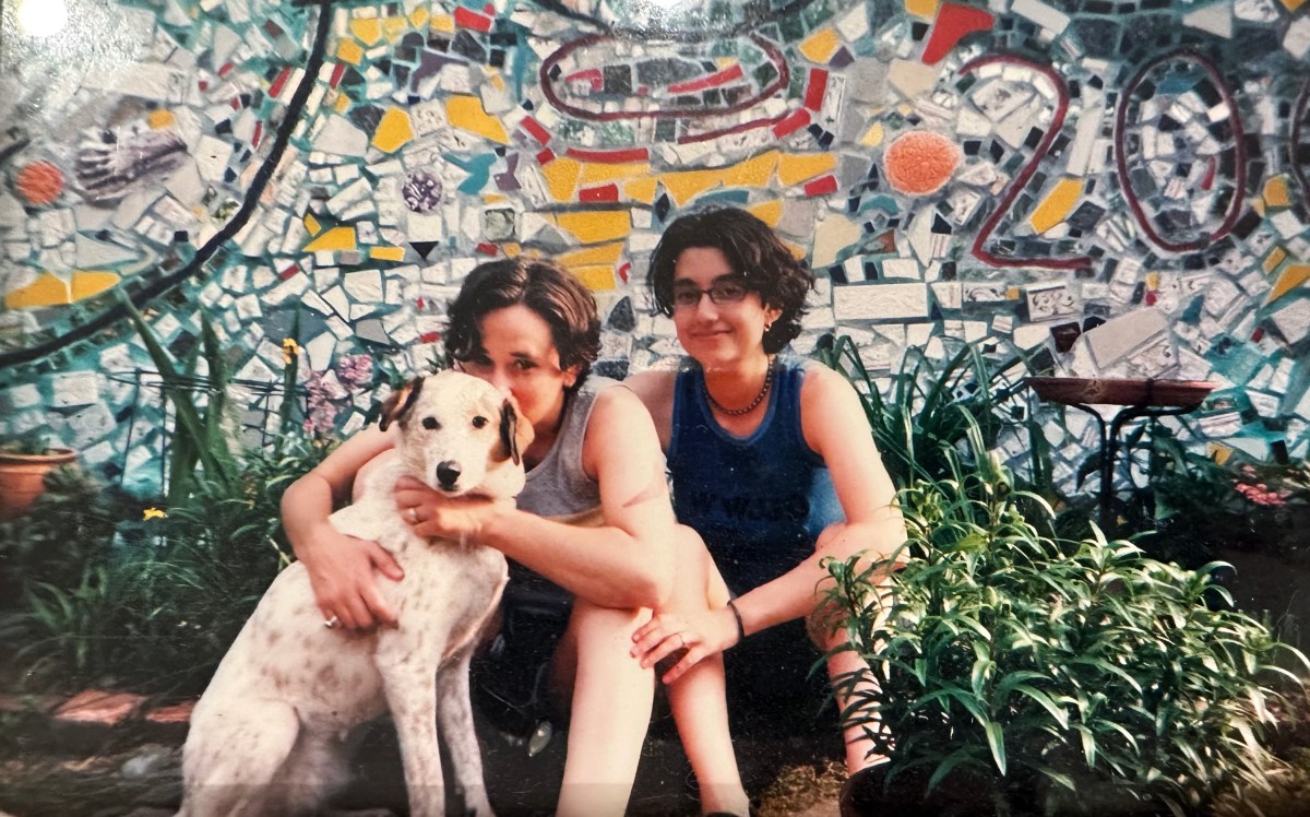 In this older photo, Tracy and Mia pose in front of a colorful mosaic while holding a very cute medium-sized dog.