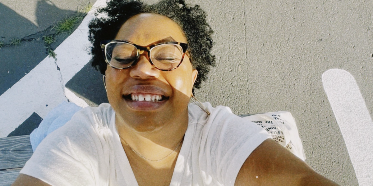 A selfie of Carmen taken from above, she is smiling and in a parking lot, she's wearing a white t-shirt