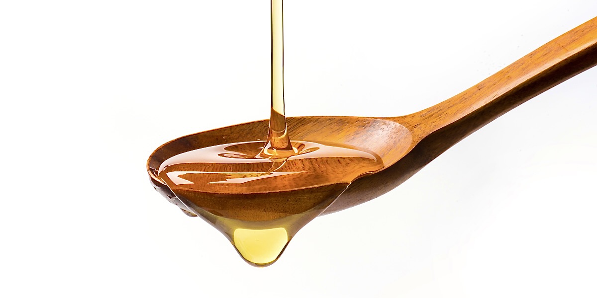 A wooden spoon in front of a white background with gold oil/lube dripping off the side.