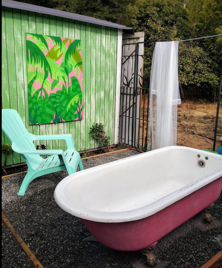a big red bathtub on an outdoor patio, with an aqua chair next to it and a beautiful print of green leaves hanging next to it