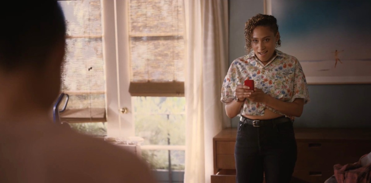 Sophie in a button-up short sleeved floral crop top and black jeans, holding an open jewelry box in amazement