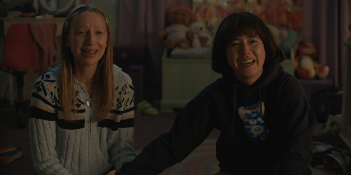 Maya Erskine and Anna Konkle hold hands and laugh cry looking up at a screen in the final moments of Pen15.