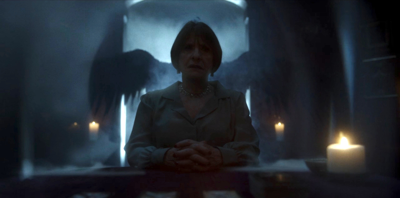 Patti LuPone in darkness has angel wings behind her.