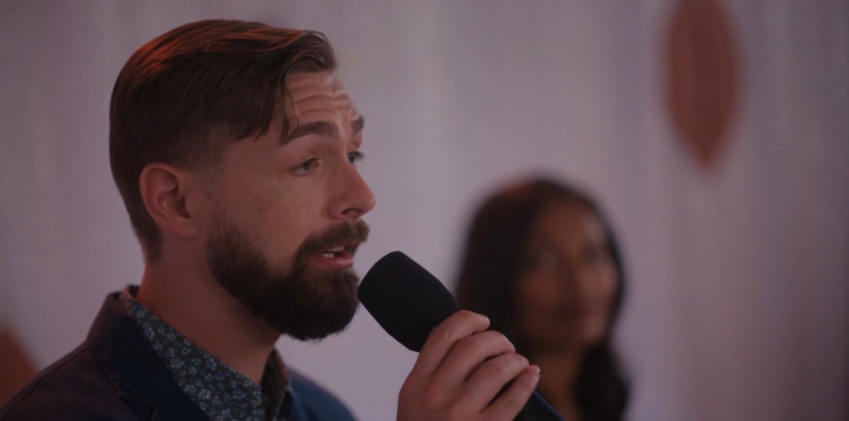 White man with a beard holding a microphone and speaking