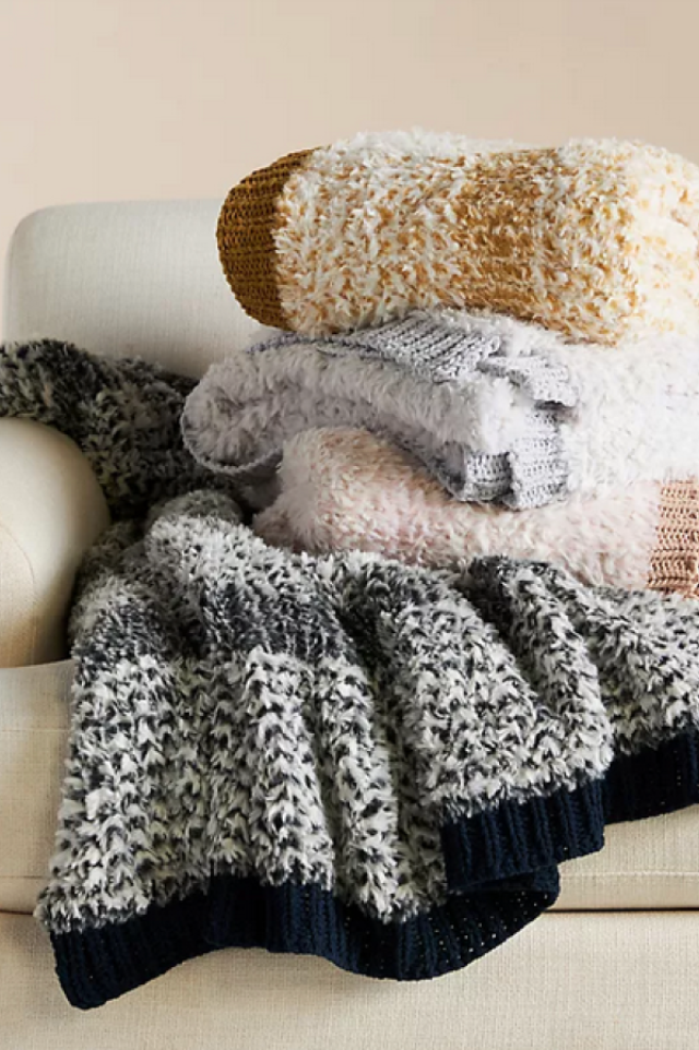 four woven blankets: black and white, pink and white, gray and white and yellow and white on a cream couch against a beige wall
