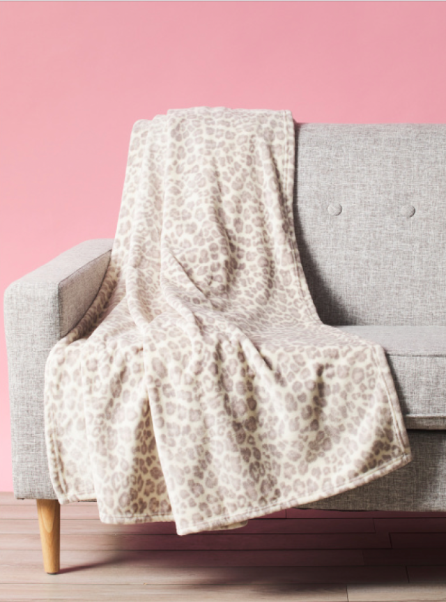 a gray and white leopard print blanket on a gray couch against a pink wall