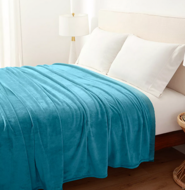a teal blanket draped over a white bed with big white pillows against a white wall