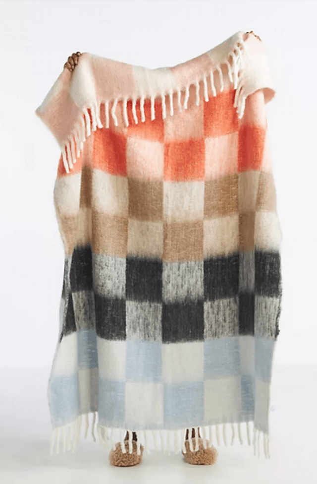 hands holding up a white blanket with tan, orange, light blue and black checkered pattern