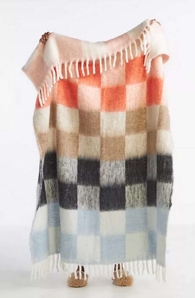 hands holding up a white blanket with tan, orange, light blue and black checkered pattern