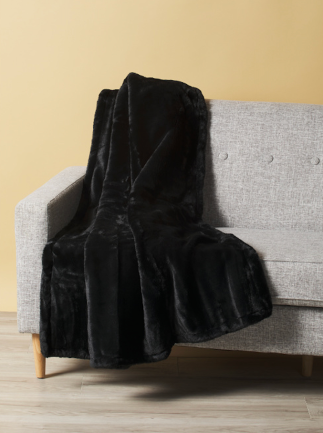 a thick black blanket draped over a gray couch against a yellow wall