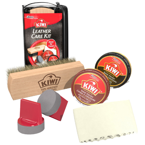 Against a white background, there is a black and red plastic zip pouch, which reads, "Kiwi Leather Care Kit." In front of the pouch, there is a shine brush (which reads, "Kiwi"), two grey sponges with red plastic handles, a tin of brown polish with a red label reading, "Kiwi," a tin of black polish with a red label reading, "Kiwi," and a light yellow cleaning cloth.