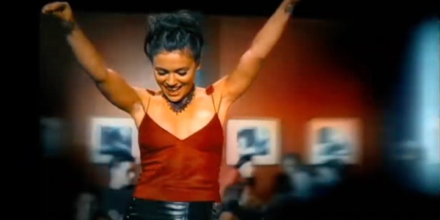 Alyssa Milano in the 00s in a red tank top dancing on a bar table, her hair is pulled back in butterfly clips away from her face