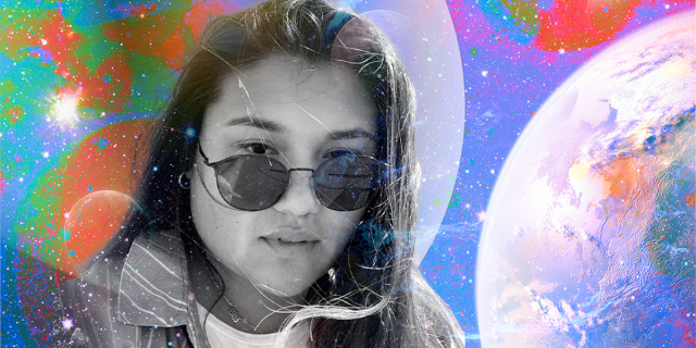 a photo of Em is set in black and white against a colorful spacey background. Em is a mixed race Asian human with long dark hair, wearing sunglasses and a jacket in this photo, looking a little windswept. They have a serious expression.