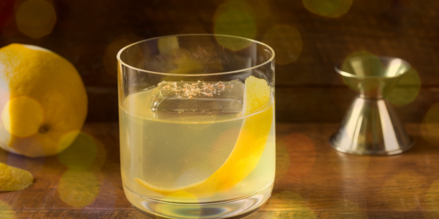 A glass of clarified milk punch with a lemon peel in it