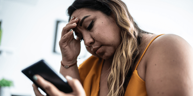 A woman with ombre hair looks at her phone, worried