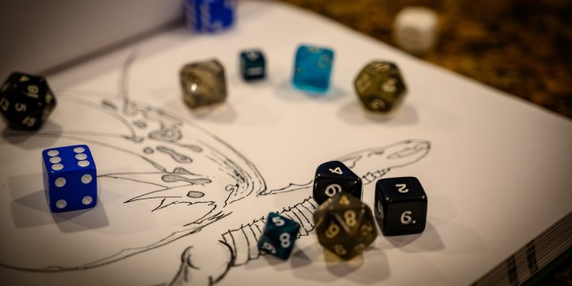 dice in many different colors are sprawled across a piece of paper with a dragon image drawn on it