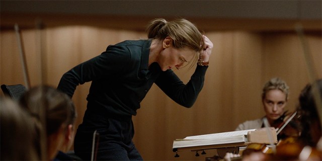Cate Blanchett as Lydia Tar, clutching her fist while directing, in a pristine black button-down shirt