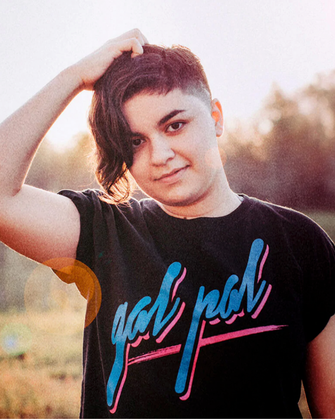 Model Marisa is wearing the Gal Pal Black Tee in size M. She is 5'3" and her bra size is 36C. The tee is black and has a graphic that says "gal pal" in retro 80s grafitti cursive typeface. The text is neon blue with a black outline and neon pink drop shadow. The text is underlined by a swipe of pink to resemble paint.