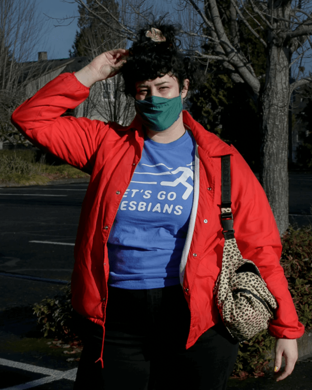 Model Nitro is wearing the Let’s Go Lesbians Tee in size L. She is 5'11" and her bra size is 34D. The shirt is sky blue with a white graphic of a stick figure posed as if on the run. Below the figure is the text "Let's Go Lesbians" in all caps and italics.