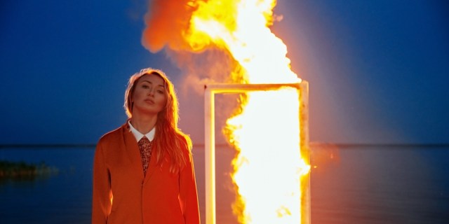 An Asian woman in a three piece suit standing in front of the burning door at the sea.