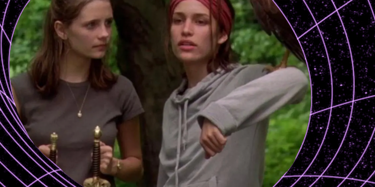 A film still from Lost & Delirious where one girl stands on the left holding two swords by the hilt and looks quizzically at the girl on her right, who's wearing a red sweatband over her forehead and hoisting a falcon on her arm. the still is within a cyberspace style black hole