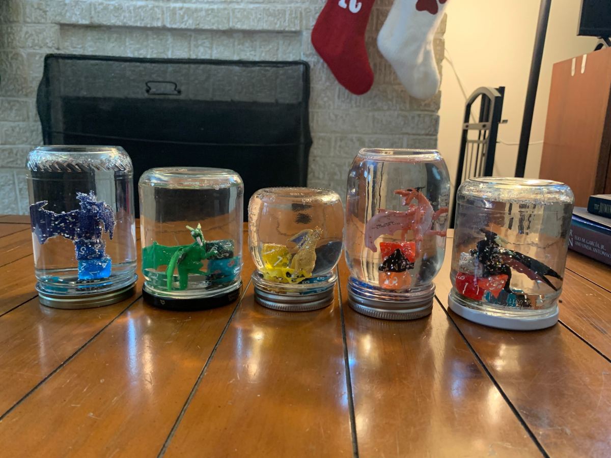 a line of four homemade snow globes each with a loose dragon and dice in them