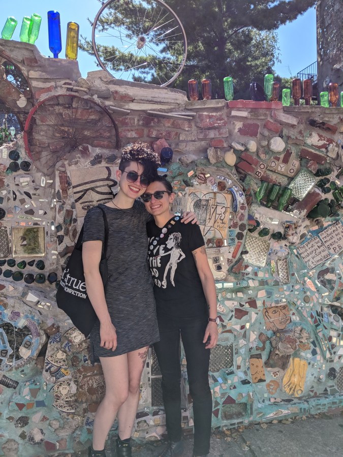sadie and nico pose on a sunny day in front of the wall to the magic garden in philadelphia