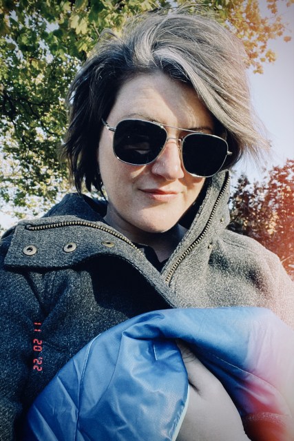 Autostraddle writer Meg Jones Wall takes a selfie outside, on a crisp, cold day, holding her new insulated blanket from REI