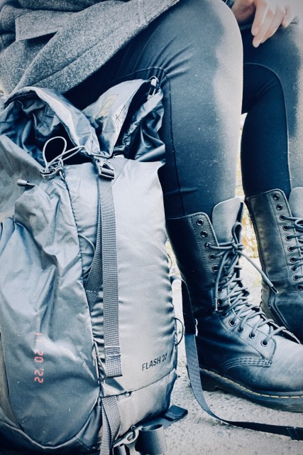 A black, outdoorsy backpack from REI rests on the ground next to Autostraddle writer Meg Jones Wall's feet, in black combat boots