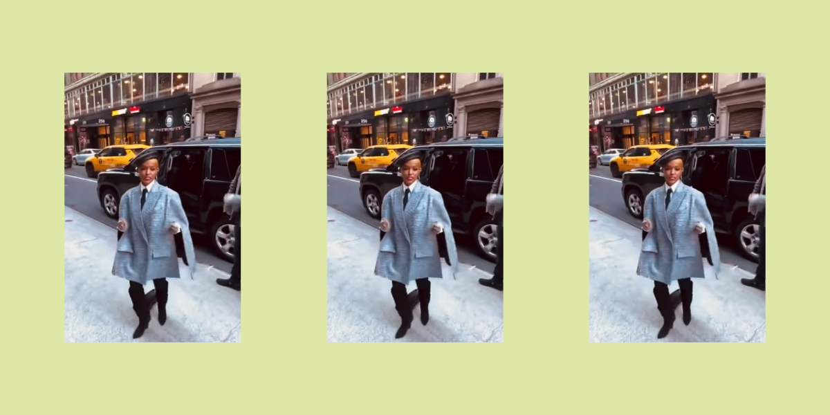 Janelle Monáe stands on a sidewalk wearing a gray coat and a beret