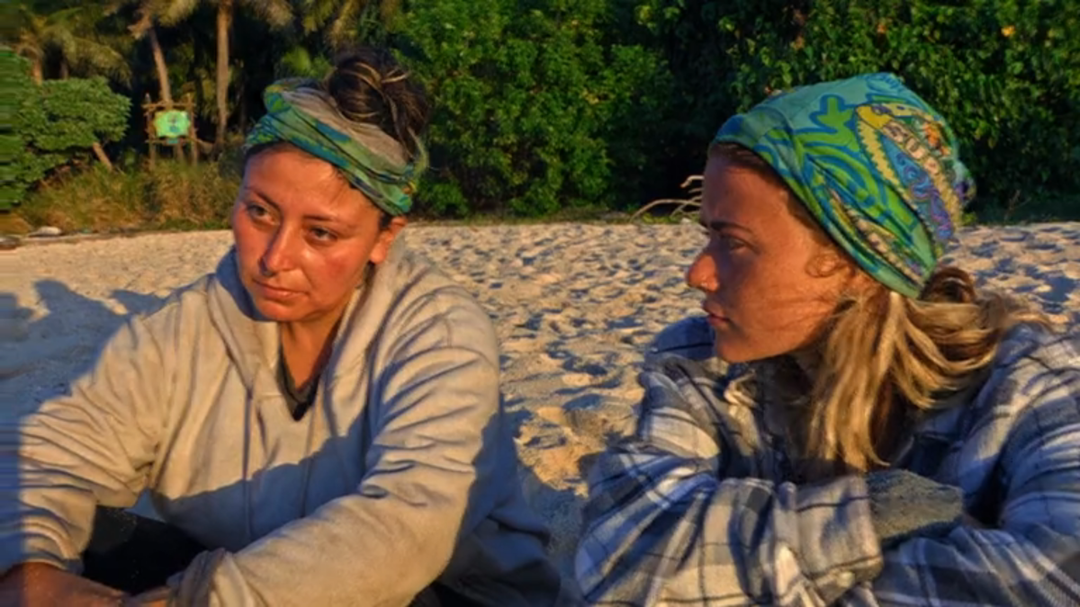 Karla Cruz Godoy, a contestant on Survivor 43, sits on the beach looking mournful next to another contestant, Cassidy