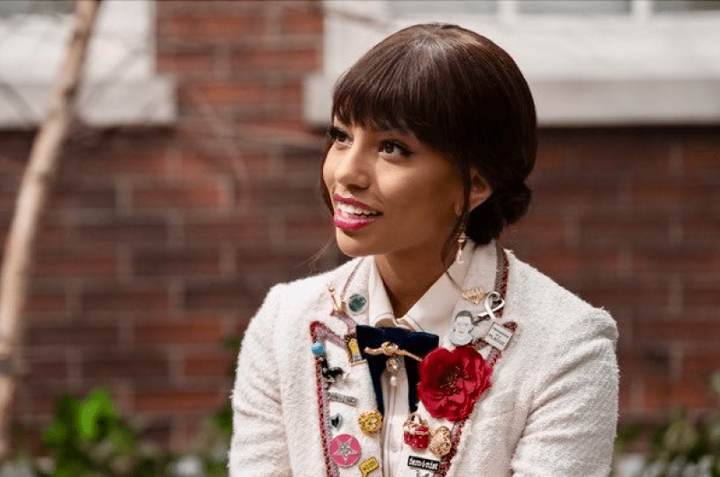 Monet de Haan dressed in a white blazer and a lapel full of pins, smiling off to the right of camera