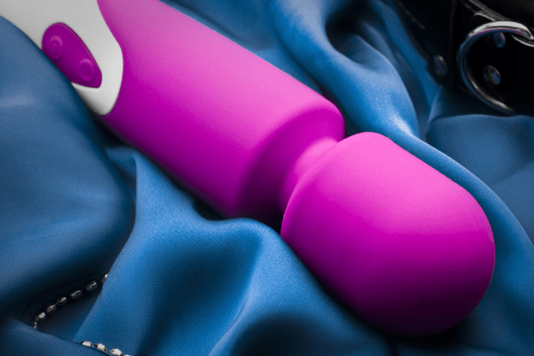 A pink and white wand vibrator is resting on a blue sheet.