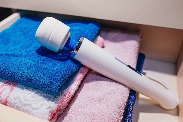 A white Magic Wand vibrator with blue buttons rests against a pile of blue, white, orange, and pink towels in a drawer.