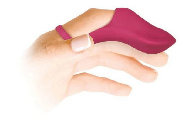 A white person's hand with a French manicure is in a relaxed position. On the pointer finger, there is a magenta vibrator that fits over the top of the finger and wraps around the base of the finger like a ring.