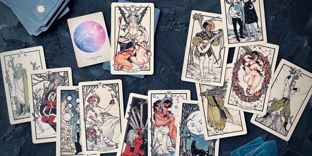 A collection of tarot cards are spread out over a dark navy blue wood tabletop.