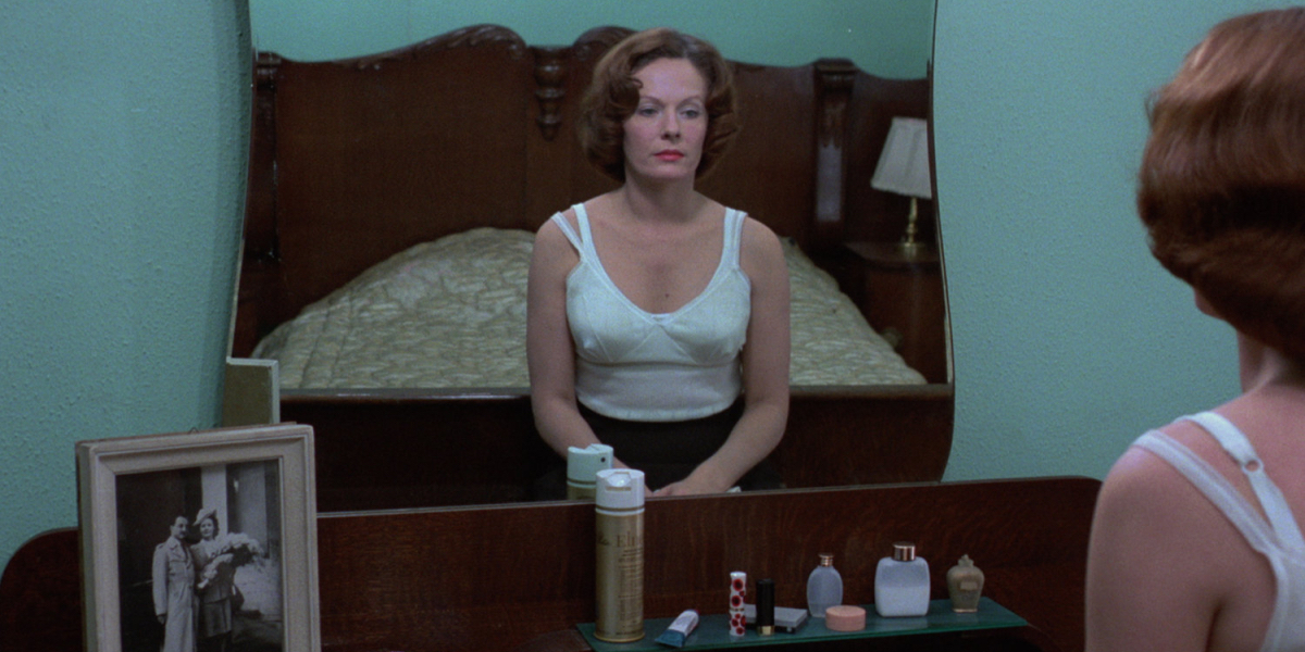 Delphine Seyrig in Jeanne Dielman looks in a mirror wearing only an undershirt.