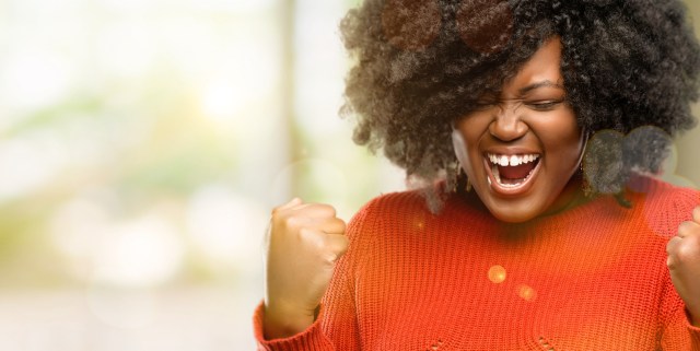 a Black woman wearing a red sweater smiles a huge joyful smile